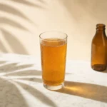Copo de vidro com kombucha âmbar servida gelada sobre superfície de mármore branco